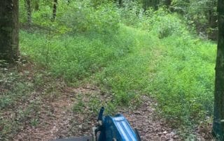 Overgrown trail that is being bush hogged by a tractor.